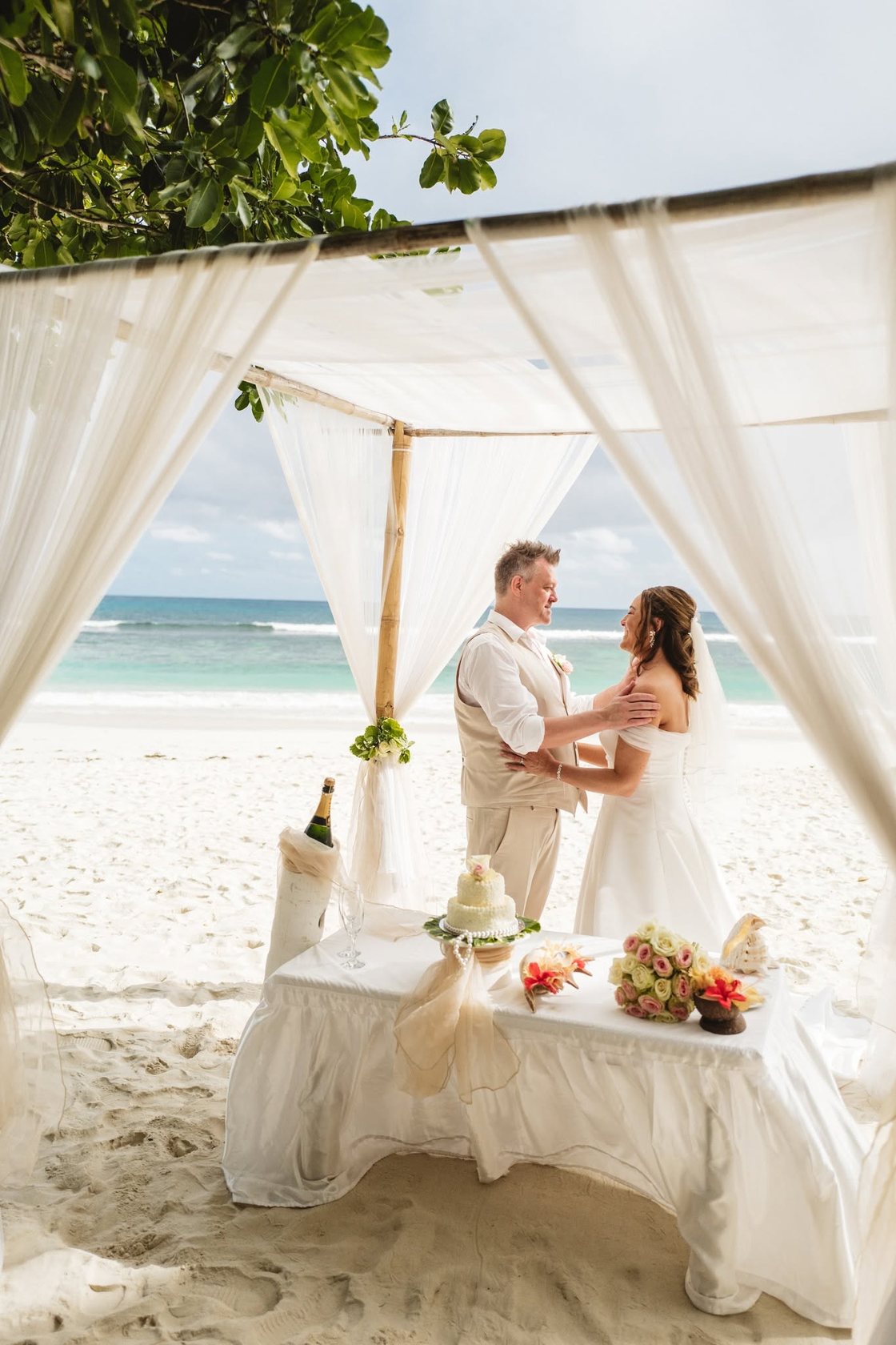 Newlyweds in a first embrace beneath white drapes on Baie Lazare beach, Mahe
