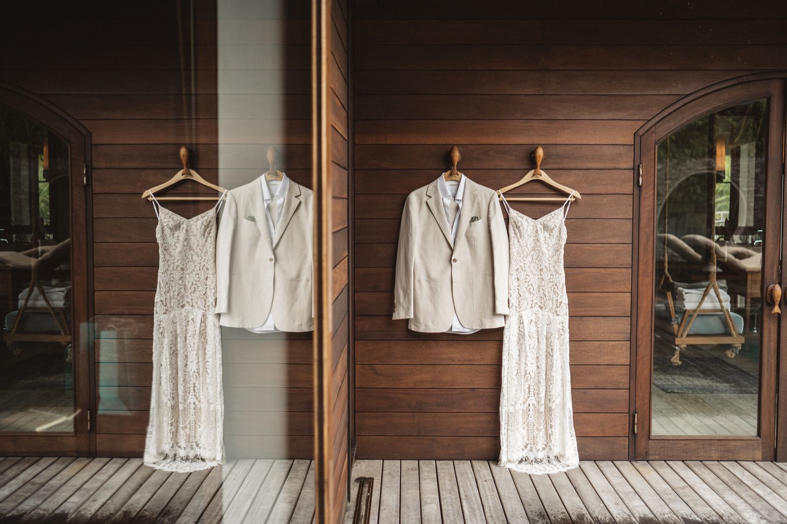 Lace wedding dress and linen jacket hanging side by side on a wooden veranda wall
