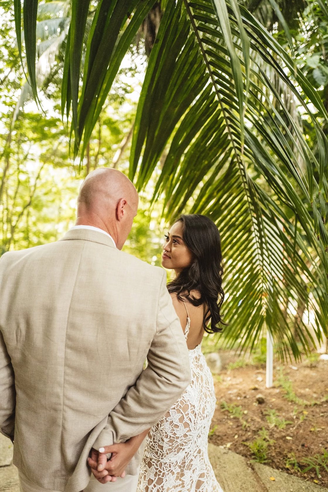 A bride glancing back at her groom beneath the palms at Constance Ephelia, Mahe