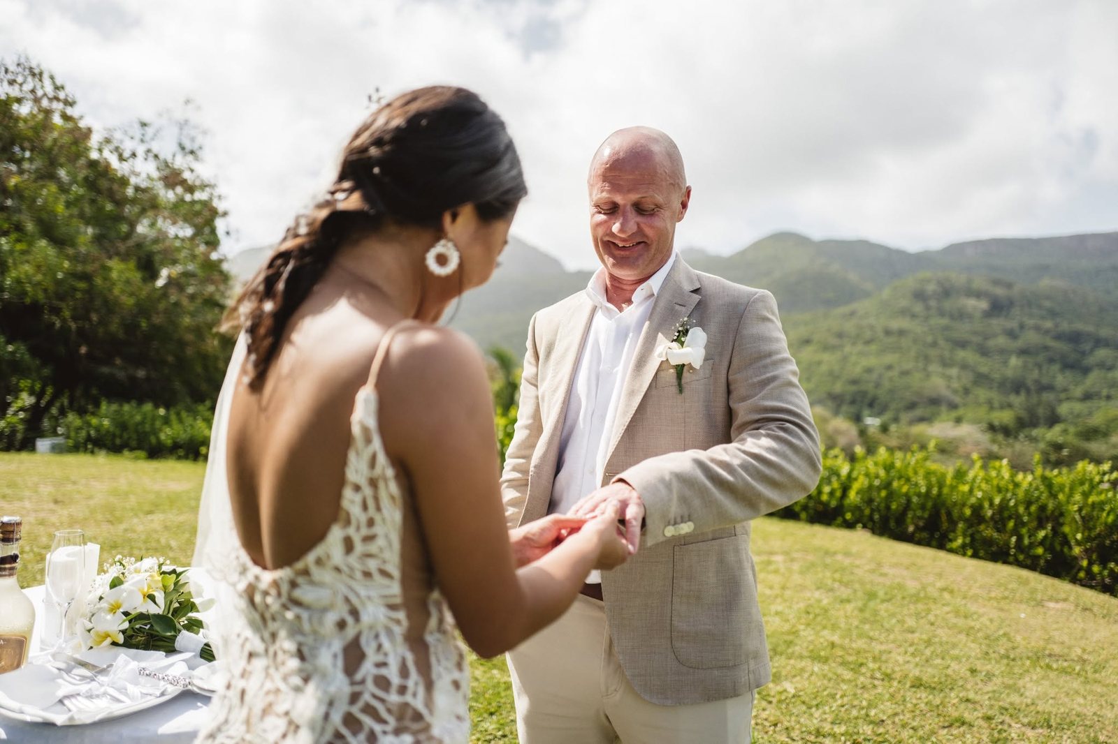 A couple exchanging rings with the green hills behind them at Constance Ephelia, Mahe