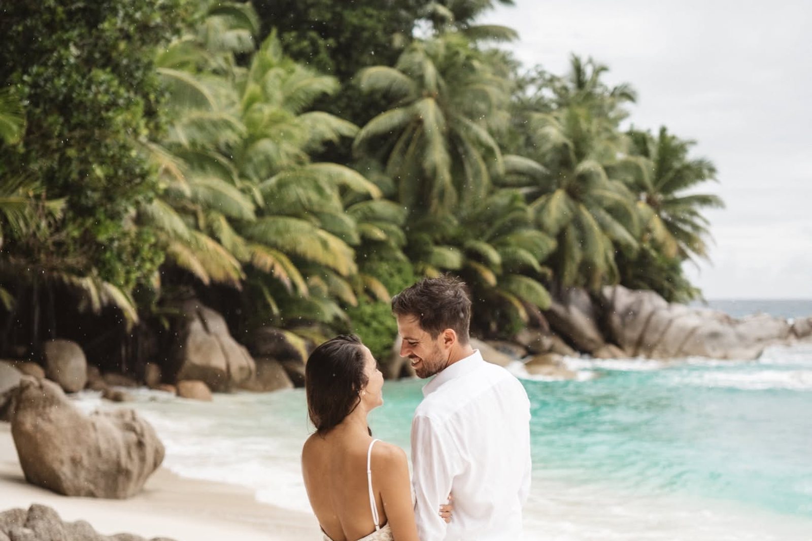 A couple on a small cove beach framed by palms and granite