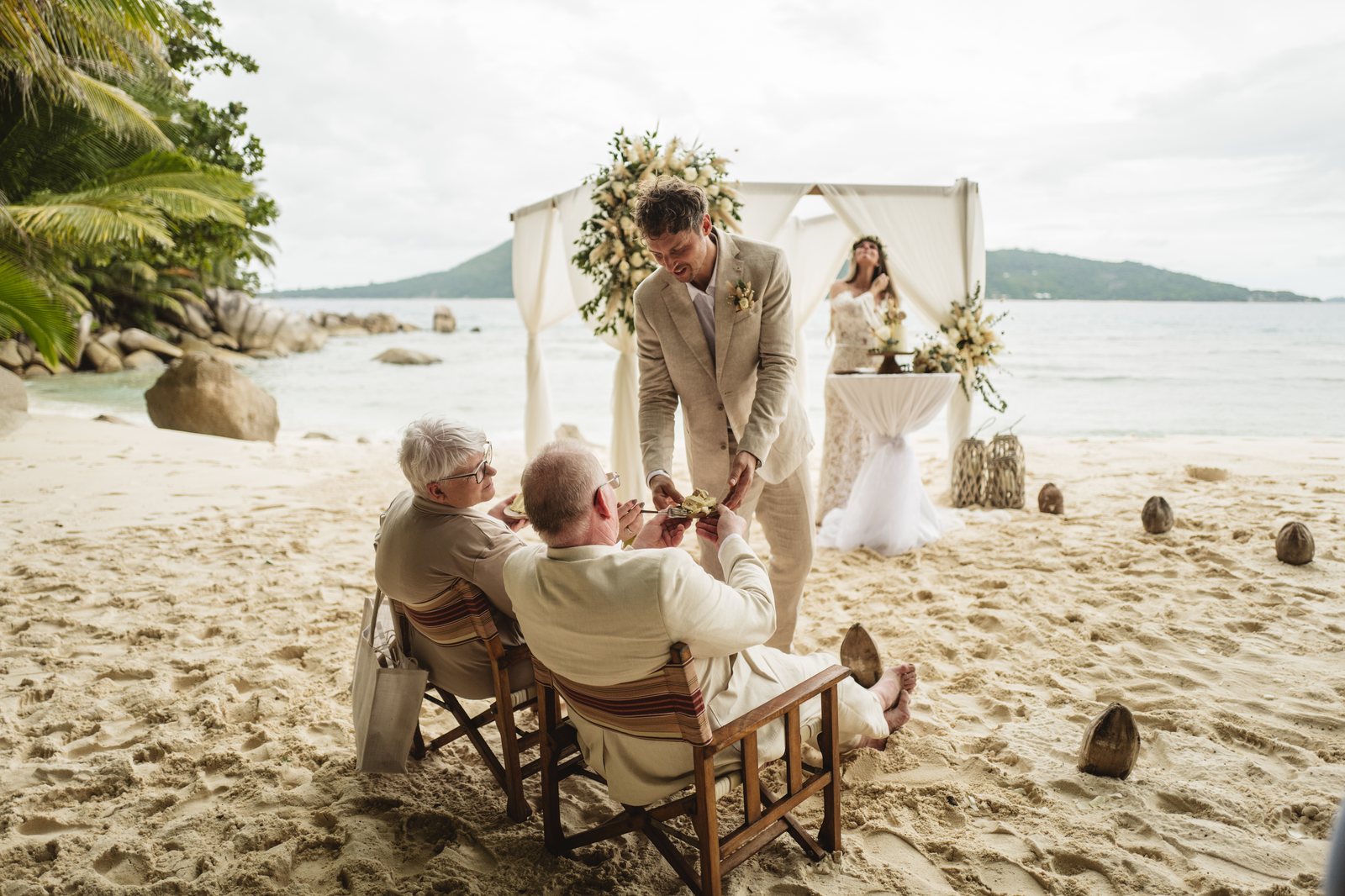 Guests seated on the sand for a ceremony under a floral arch