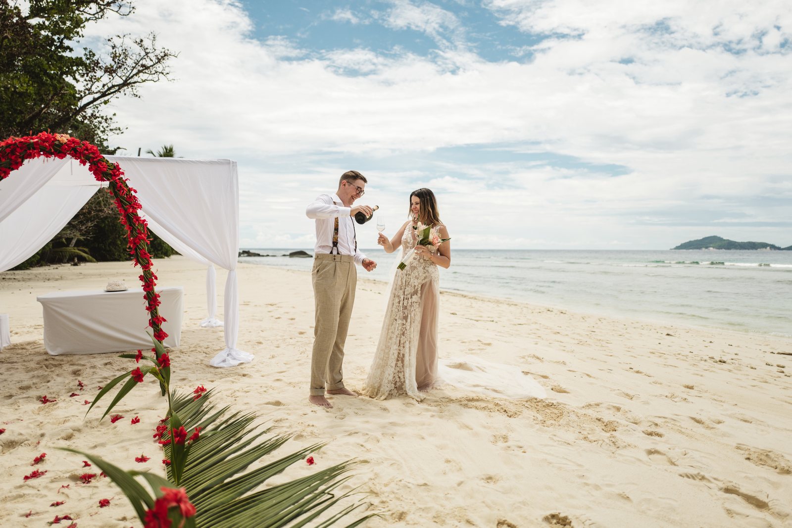 Bride and groom toasting with champagne by their flower arch on the beach at Hilton Labriz, Silhouette