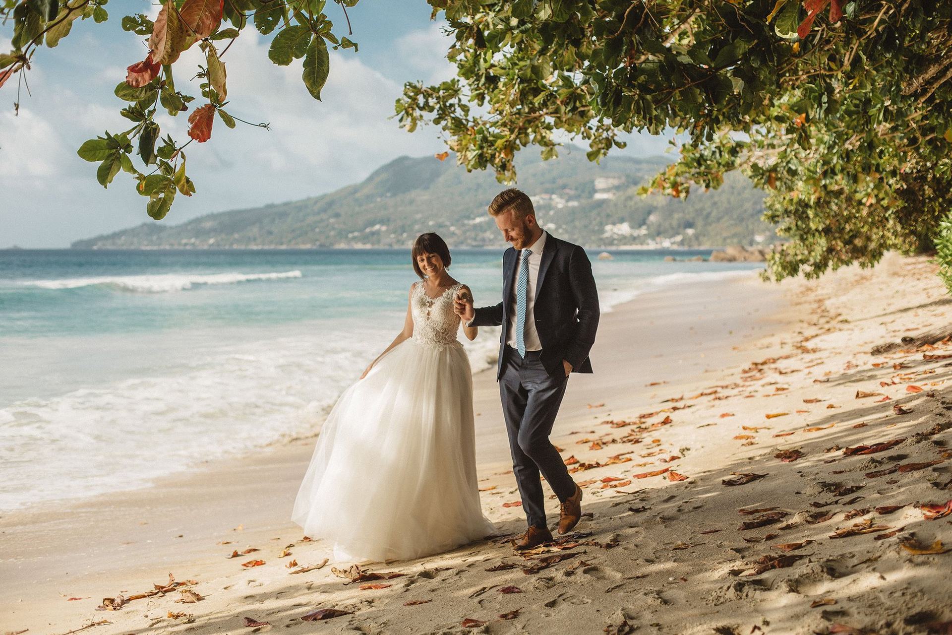 Bride and groom walking a quiet Seychelles beach under takamaka trees