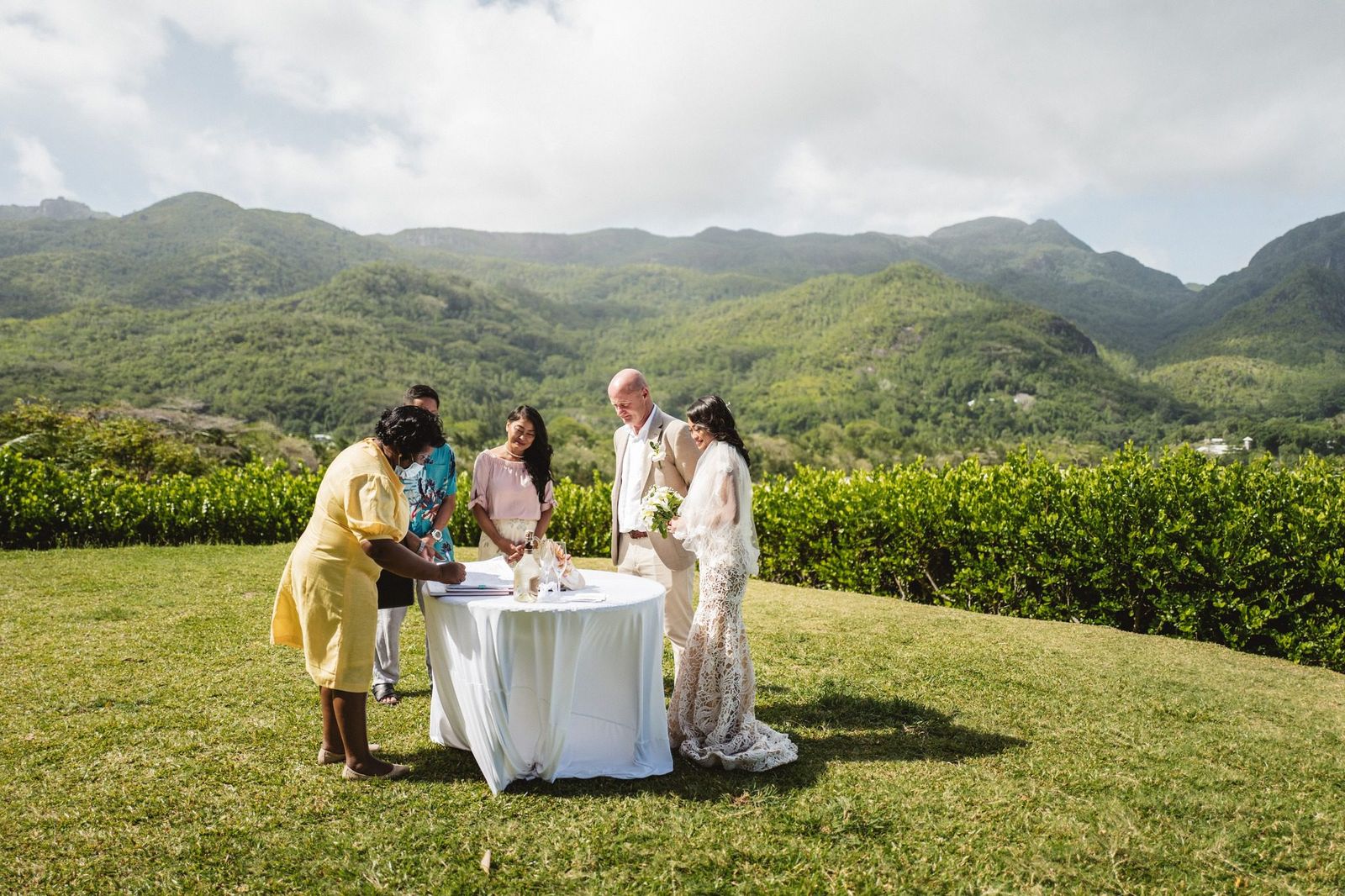 Signing at a round table on a hilltop lawn, green mountains behind