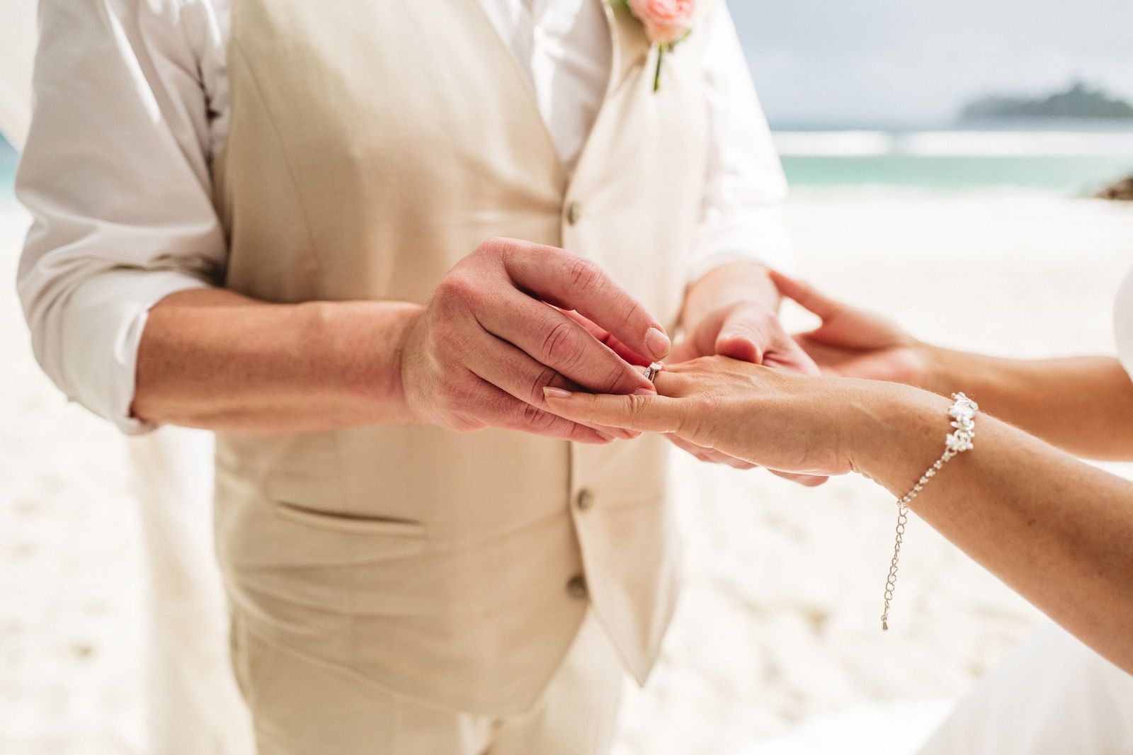 Close-up of the groom placing the ring on the bride's hand at a beach ceremony