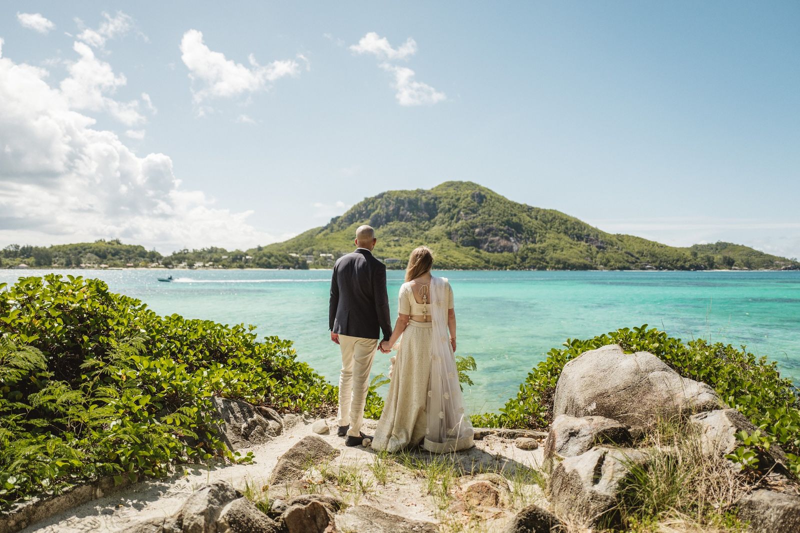 Bride and groom looking out across turquoise water to a green island hill