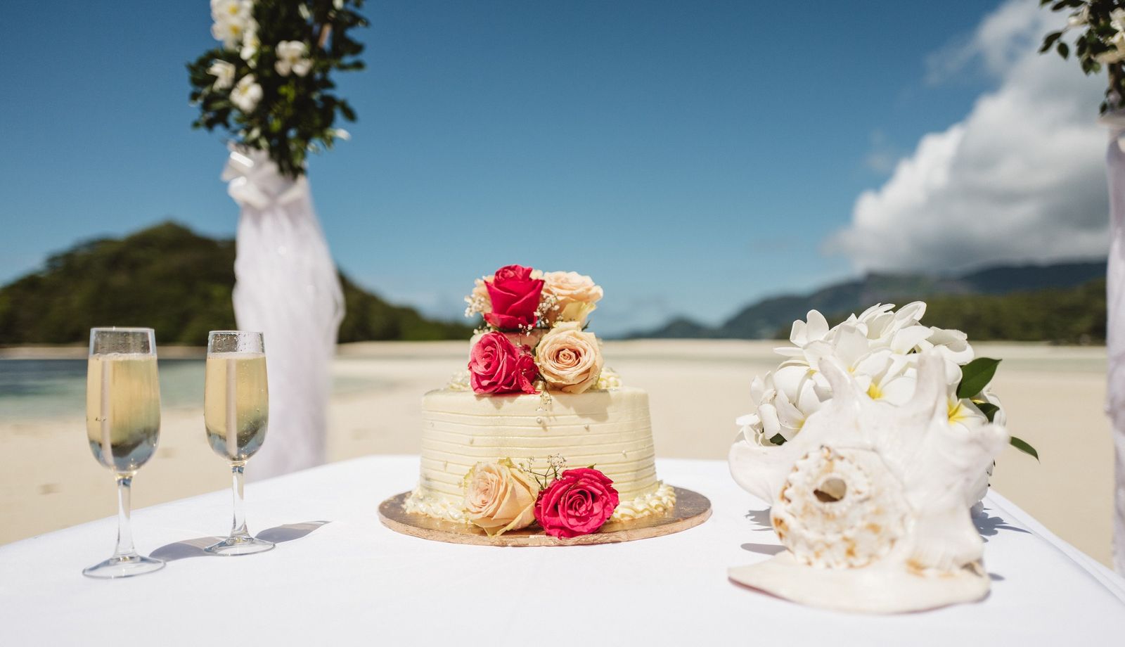 Cake, champagne flutes and the bouquet on a white table by the water