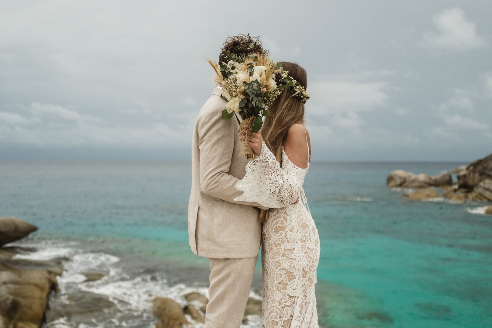 Bride and groom walking a beach scattered with takamaka leaves