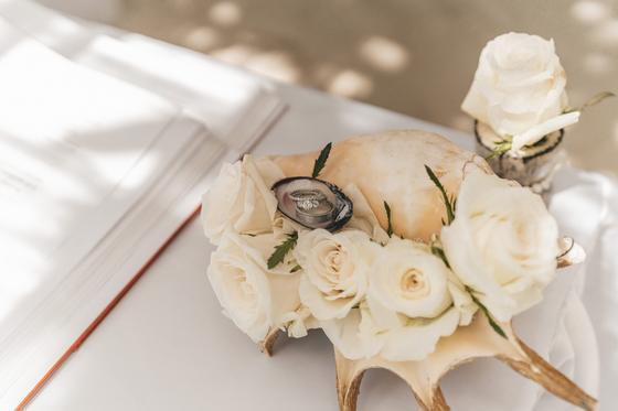Wedding rings in an oyster shell on a coconut casket ringed with white roses