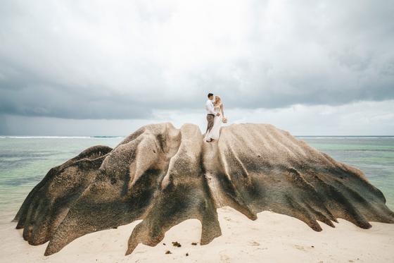 Bride and groom standing on a huge sculpted granite outcrop at low tide under a moody sky