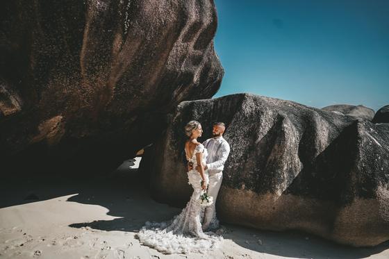 Bride in a feathered train against dark sculpted boulders
