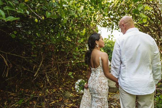 Hand in hand on a path through dense green, her lace back to the light