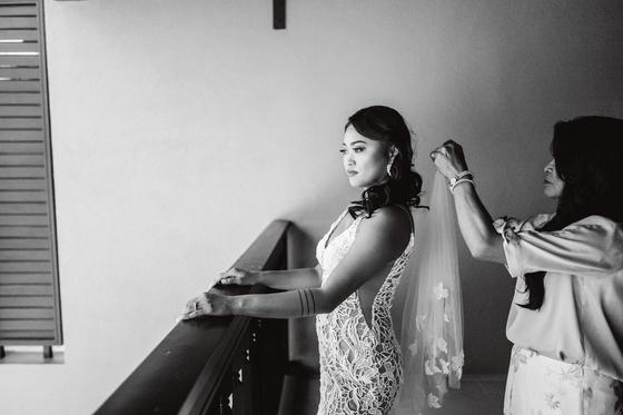 Bride at a window while her veil is set in place, in black and white
