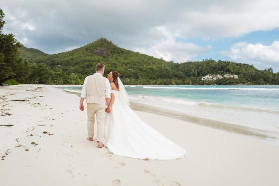 Walking the shoreline, the veil and train trailing on wet sand