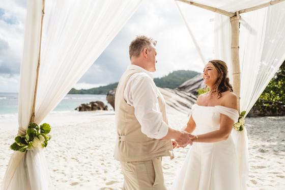 Vows under a bamboo gazebo with white drapes on an empty beach