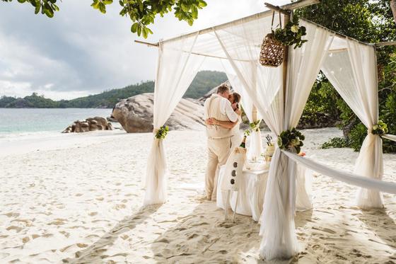 A kiss under the full canopy of a draped beach gazebo