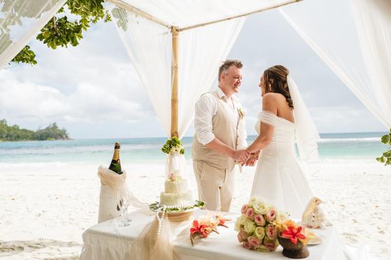 Holding hands across the ceremony table, cake and tropical flowers set out