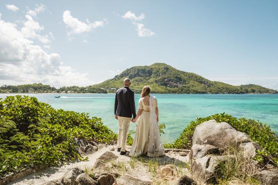 Bride and groom looking out across turquoise water to a green island hill