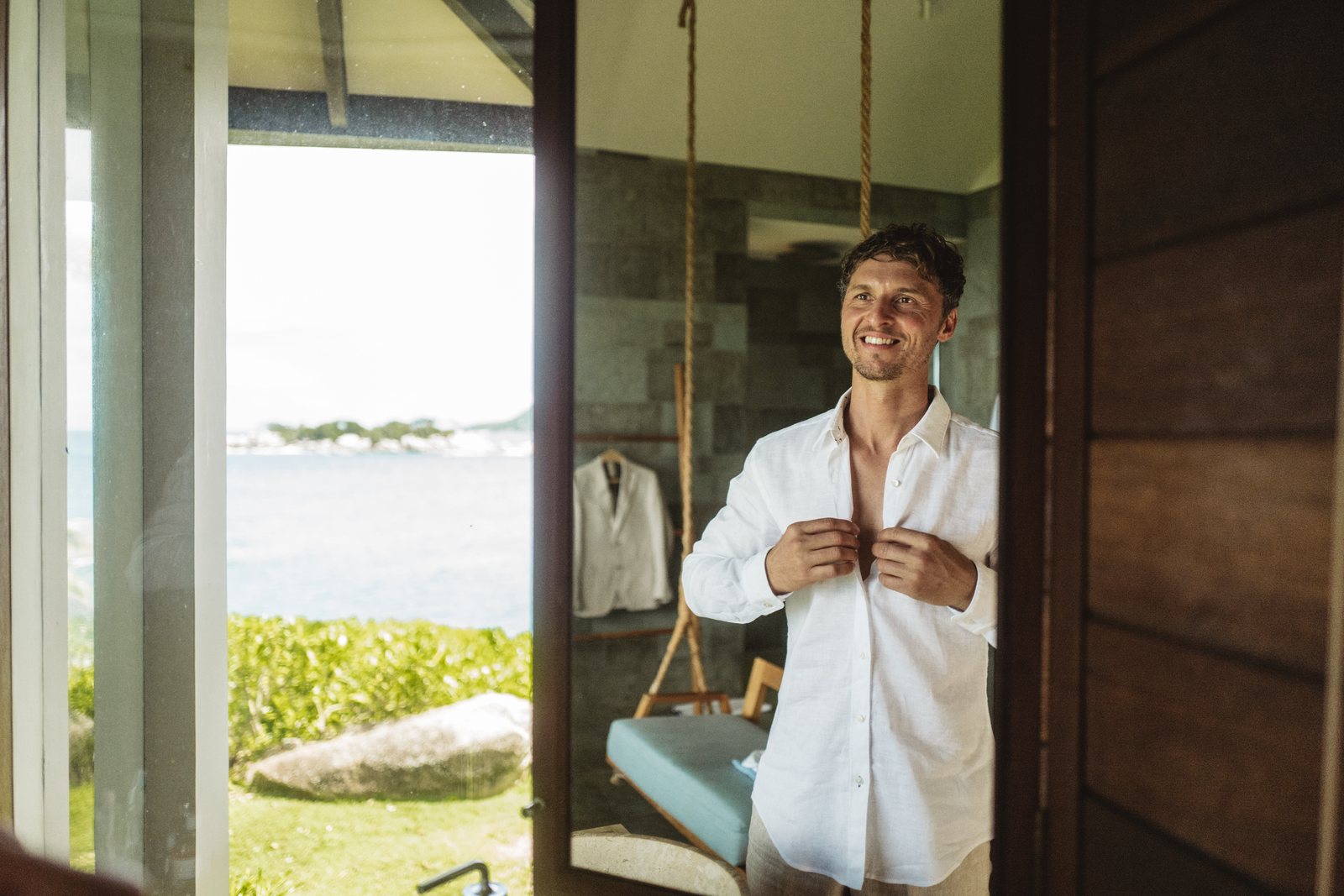 A groom buttoning his shirt with the sea behind him, Six Senses, Felicite
